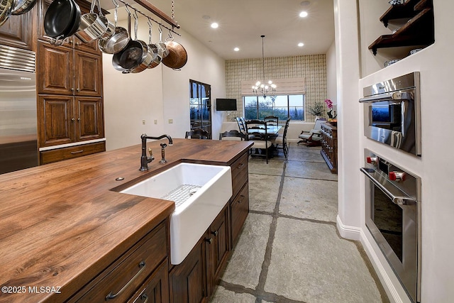 kitchen featuring butcher block countertops, appliances with stainless steel finishes, an inviting chandelier, a sink, and recessed lighting