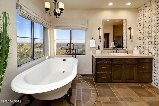 full bathroom with a chandelier, a freestanding tub, vanity, and recessed lighting