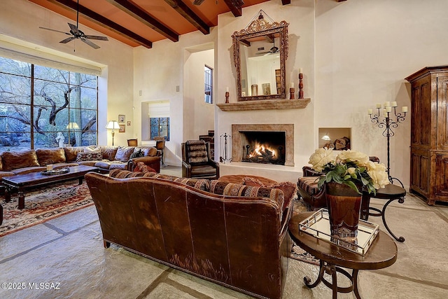 living area with beamed ceiling, a high end fireplace, a towering ceiling, and a ceiling fan