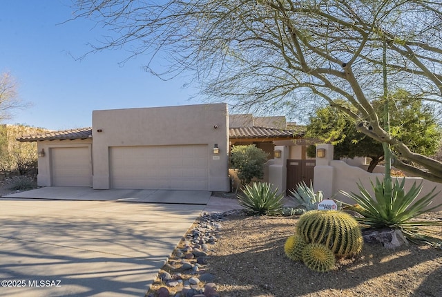 pueblo-style home featuring a garage, driveway, a tile roof, and stucco siding