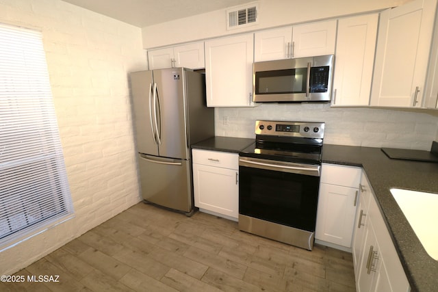 kitchen featuring visible vents, dark countertops, light wood-style flooring, appliances with stainless steel finishes, and white cabinetry