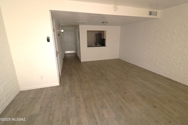 empty room featuring brick wall, wood finished floors, and visible vents