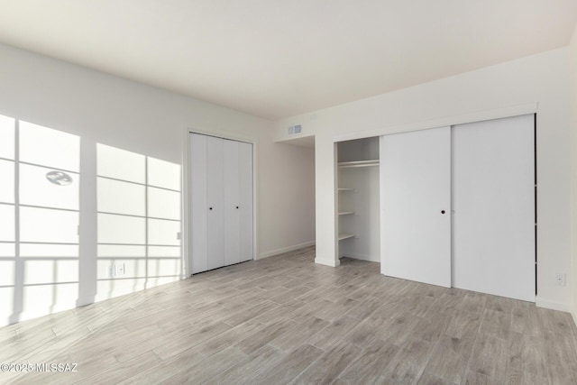 unfurnished bedroom featuring visible vents, light wood finished floors, and two closets