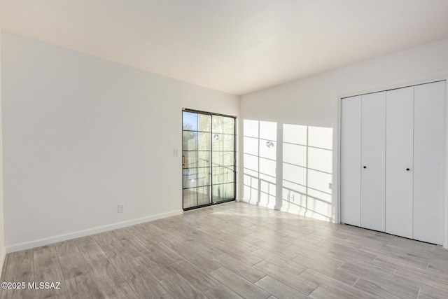 unfurnished bedroom featuring light wood-style floors, baseboards, and a closet