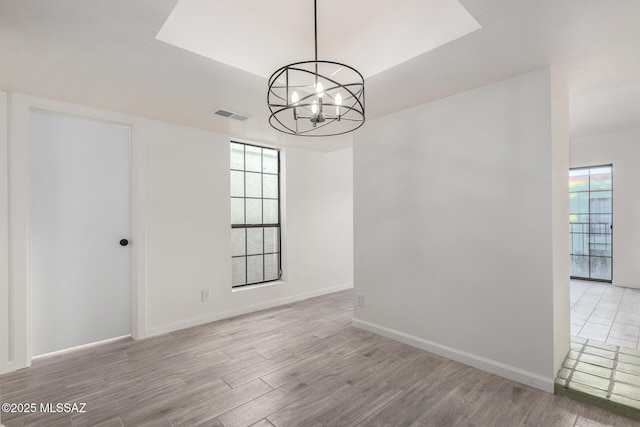 spare room featuring baseboards, light wood-style floors, visible vents, and an inviting chandelier