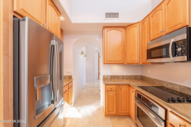 kitchen featuring visible vents, arched walkways, light stone countertops, stainless steel appliances, and light brown cabinets