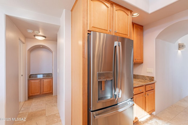 kitchen with light stone countertops, arched walkways, and stainless steel refrigerator with ice dispenser