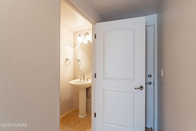 half bathroom with a textured wall and a sink