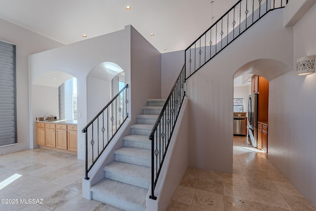 staircase with arched walkways, a high ceiling, and recessed lighting