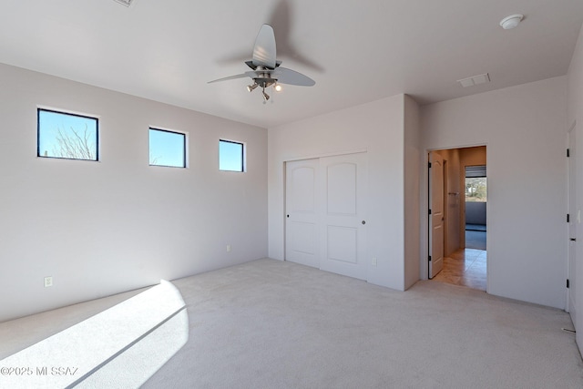 unfurnished bedroom with a ceiling fan, a closet, light carpet, and visible vents