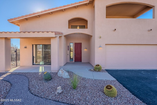 view of front of property with aphalt driveway, a tiled roof, a garage, and stucco siding