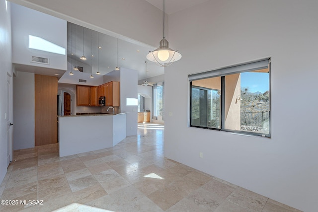 kitchen featuring a high ceiling, brown cabinetry, appliances with stainless steel finishes, and visible vents