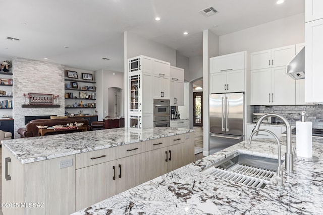 kitchen with visible vents, arched walkways, open floor plan, a sink, and built in fridge