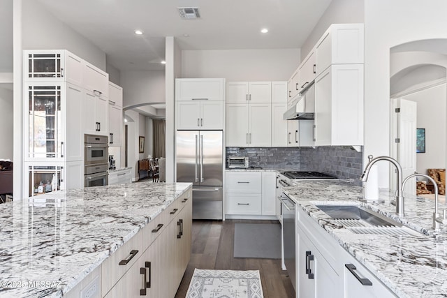 kitchen with arched walkways, stainless steel appliances, visible vents, a sink, and light stone countertops