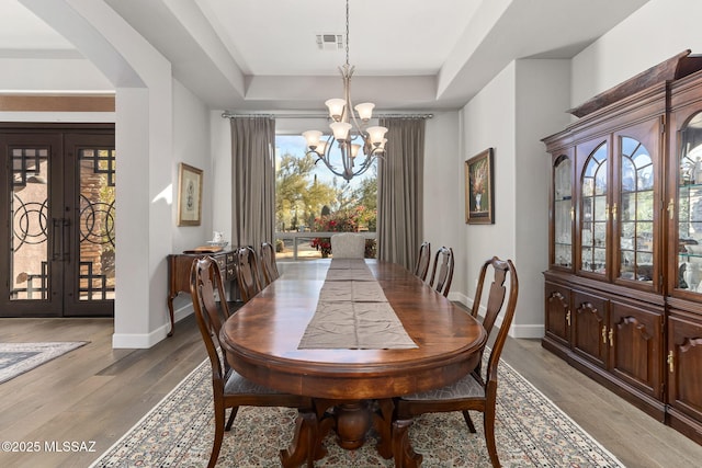 dining space with a chandelier, a tray ceiling, light wood-style flooring, and visible vents