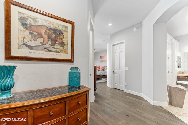 hall featuring light wood-type flooring, arched walkways, and baseboards