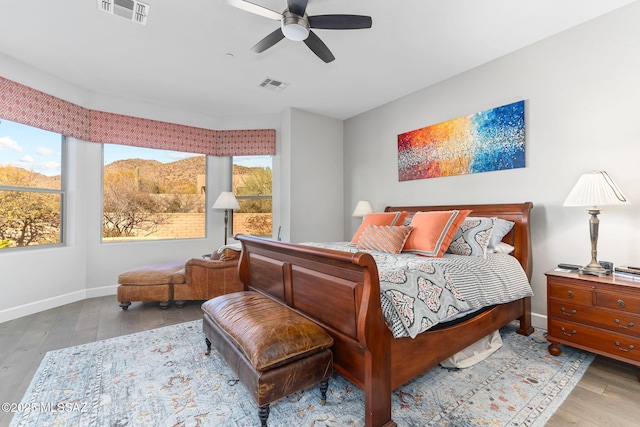 bedroom with a ceiling fan, visible vents, baseboards, and wood finished floors