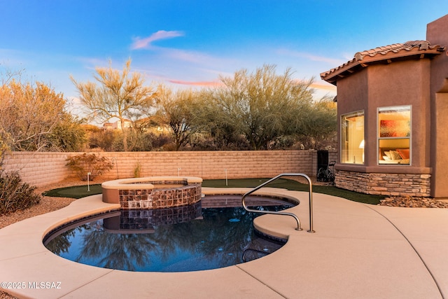 pool at dusk featuring a pool with connected hot tub and fence