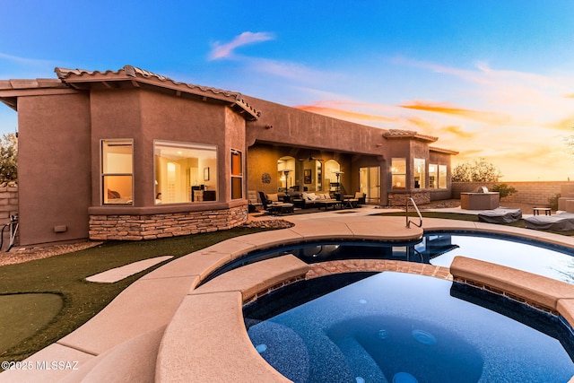 back of property at dusk with a patio area, stone siding, fence, and stucco siding