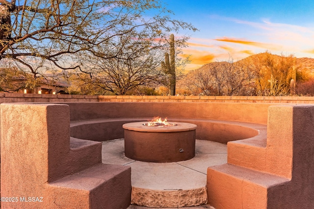 patio terrace at dusk with a mountain view, a fire pit, and fence