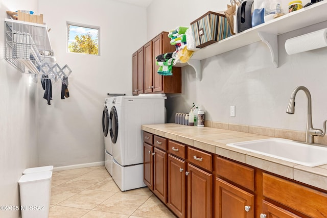 clothes washing area featuring cabinet space, light tile patterned flooring, a sink, independent washer and dryer, and baseboards