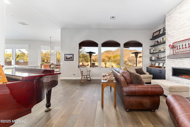 living room with built in shelves, a stone fireplace, hardwood / wood-style flooring, and visible vents