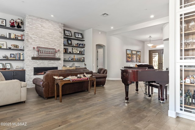 living area with visible vents, arched walkways, wood finished floors, a stone fireplace, and recessed lighting