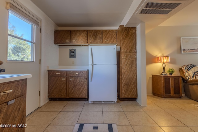 kitchen featuring light tile patterned flooring, visible vents, light countertops, freestanding refrigerator, and brown cabinetry