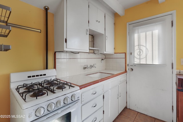 kitchen featuring tile counters, backsplash, white cabinetry, a sink, and white range with gas stovetop