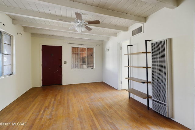 unfurnished room featuring beam ceiling, visible vents, a ceiling fan, a heating unit, and hardwood / wood-style floors