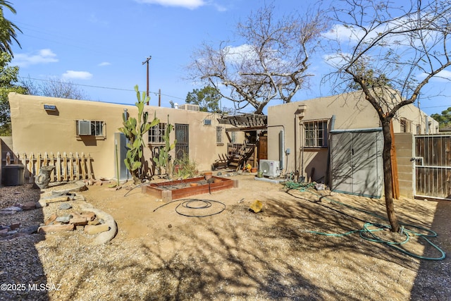 rear view of house with ac unit, a vegetable garden, fence, and stucco siding