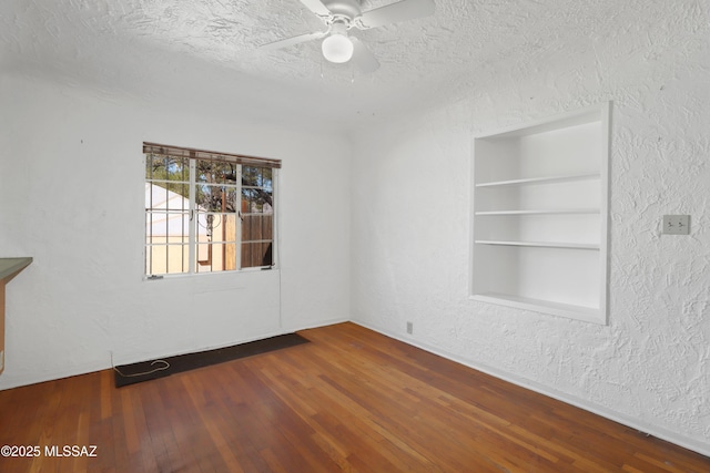 spare room featuring built in features, wood-type flooring, a textured wall, ceiling fan, and a textured ceiling