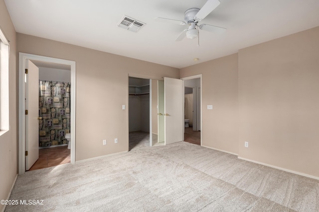 unfurnished bedroom with a walk in closet, visible vents, ensuite bath, and carpet flooring