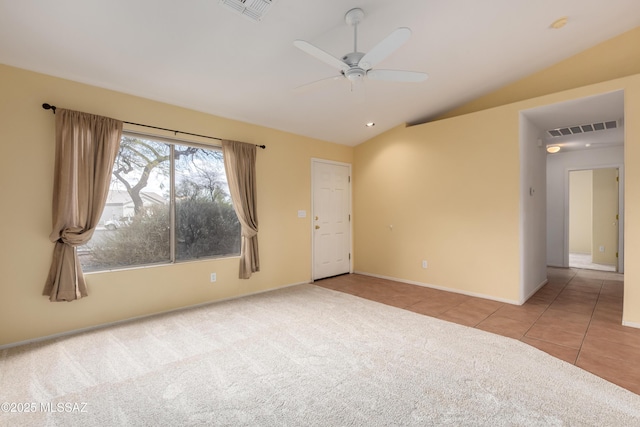 carpeted empty room with vaulted ceiling, a ceiling fan, visible vents, and tile patterned floors