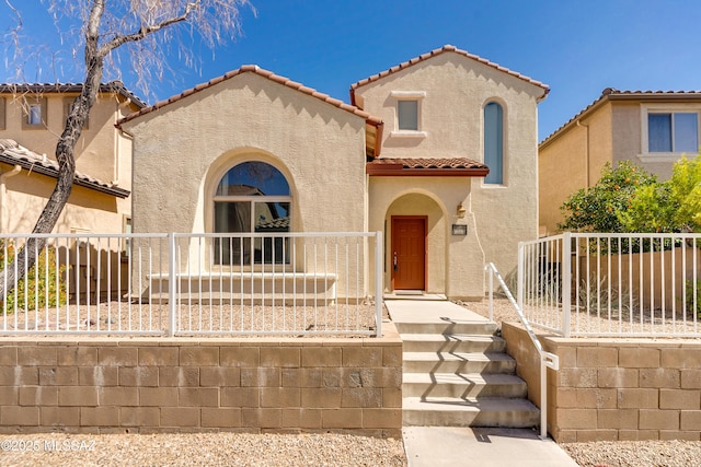 mediterranean / spanish-style home with fence, a tiled roof, and stucco siding