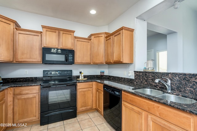 kitchen featuring brown cabinets, light tile patterned flooring, a sink, dark stone countertops, and black appliances