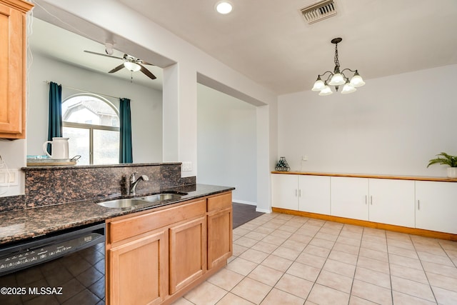 kitchen with ceiling fan with notable chandelier, a sink, visible vents, black dishwasher, and dark stone countertops