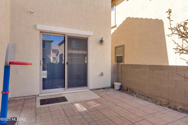 view of exterior entry with a patio area, fence, and stucco siding