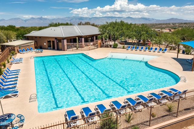 community pool with a patio area, fence, and a mountain view