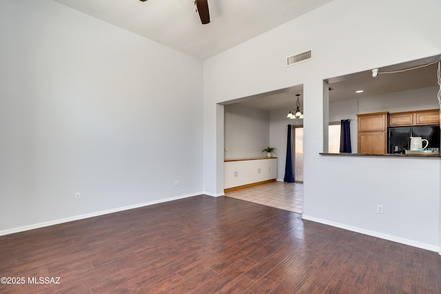 unfurnished living room with ceiling fan with notable chandelier, wood finished floors, visible vents, and baseboards