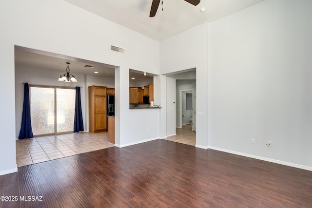 unfurnished living room with ceiling fan with notable chandelier, wood finished floors, visible vents, and baseboards