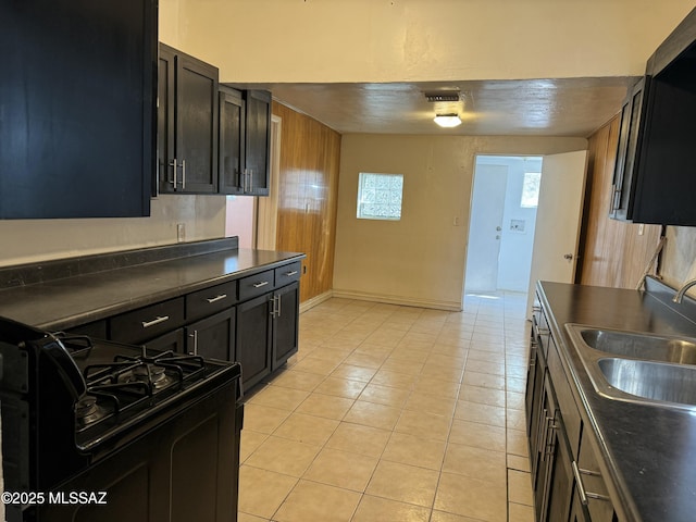 kitchen featuring baseboards, dark countertops, black range with gas stovetop, a sink, and light tile patterned flooring