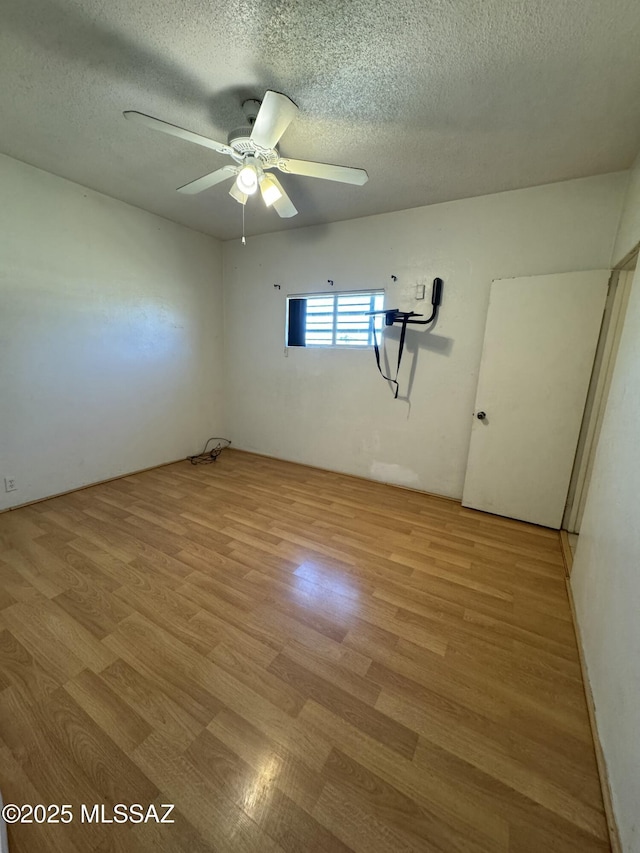 unfurnished room with a ceiling fan, light wood-style flooring, and a textured ceiling