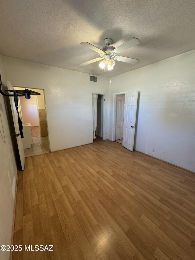 unfurnished bedroom with light wood-type flooring, a ceiling fan, visible vents, and a textured ceiling