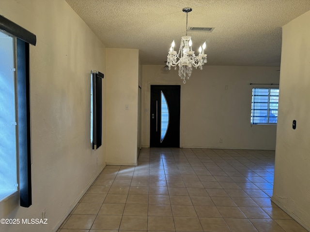 unfurnished room featuring a textured ceiling, light tile patterned flooring, visible vents, and an inviting chandelier