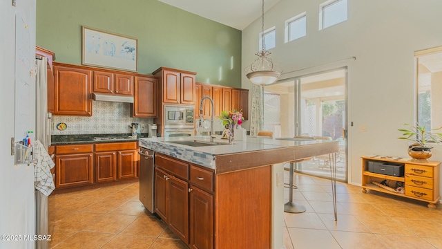 kitchen featuring an island with sink, appliances with stainless steel finishes, under cabinet range hood, a sink, and light tile patterned flooring