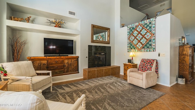 living room featuring visible vents, a towering ceiling, a tiled fireplace, tile patterned flooring, and baseboards