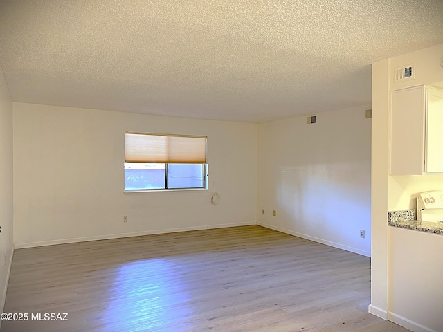 unfurnished room featuring light wood-type flooring, visible vents, and a textured ceiling