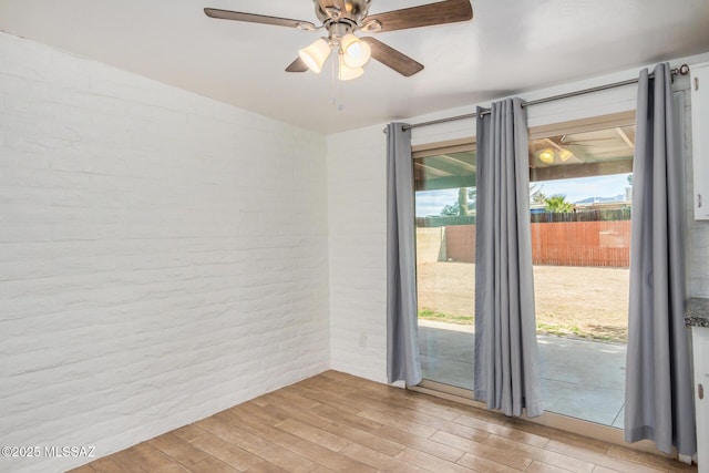 spare room featuring light wood-style floors, a ceiling fan, brick wall, and a wealth of natural light