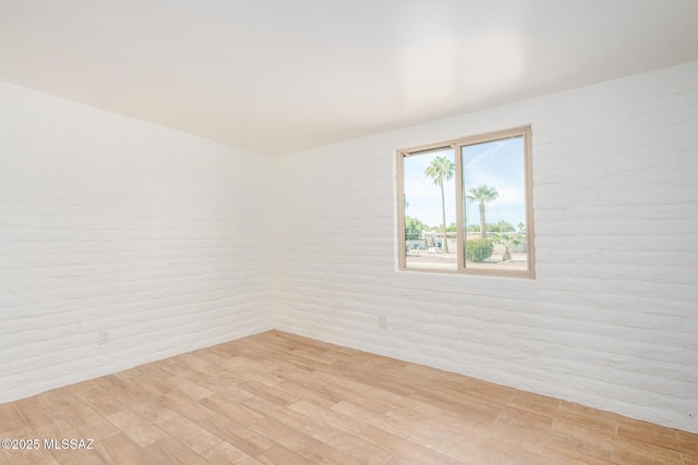 spare room with light wood-style flooring and brick wall